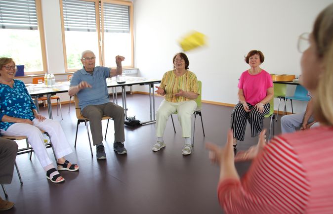 Seniorengruppe sitzt im Stuhlkreis und wirft gelbes Wurfkissen